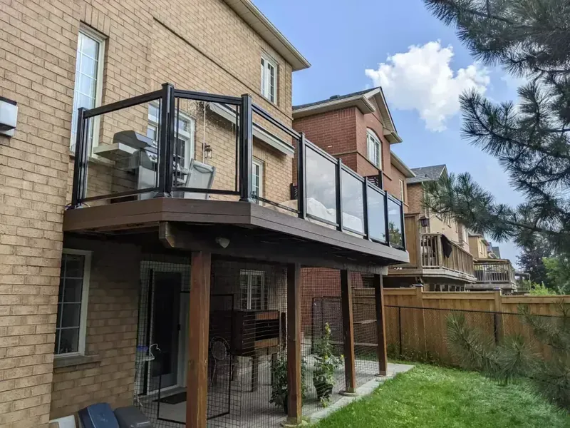 Second-storey composite deck with glass railing on a brick home, patio below