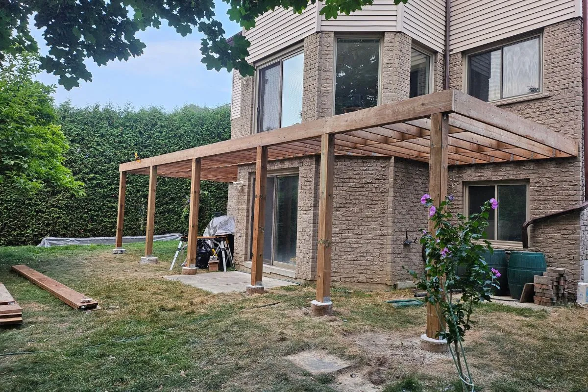 Large wooden deck frame under construction against a two-story brick house in a backyard.