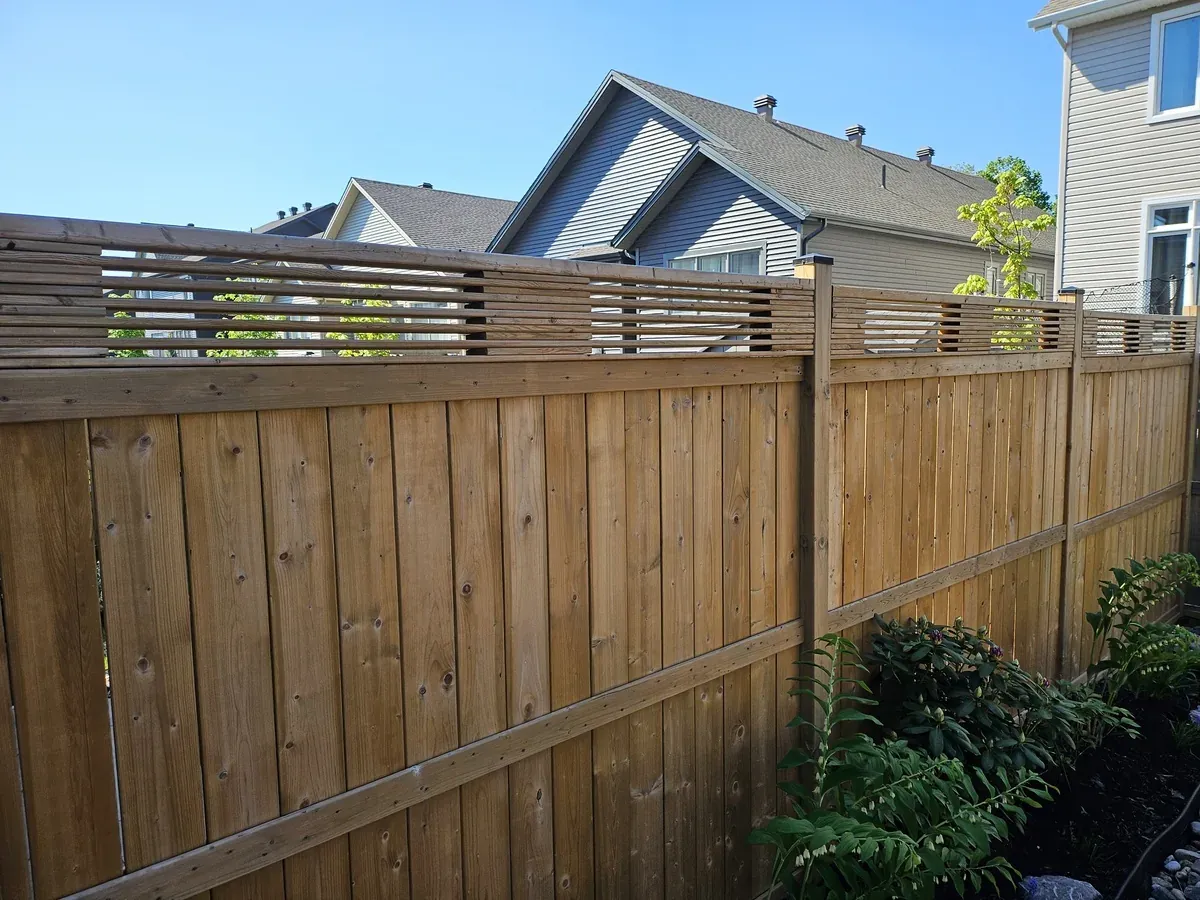 Run of pressure-treated fence panels with an open slat topper along a property line in Newmarket, with planting beds at the base