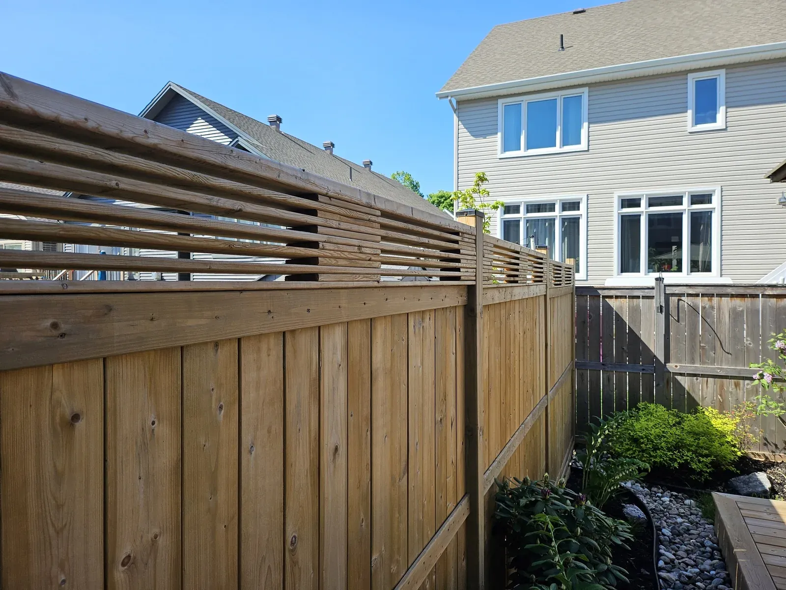 Pressure-treated privacy fence with a horizontal slat topper enclosing a back garden in Newmarket, Ontario