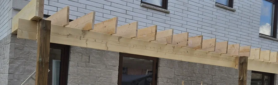 Cedar pergola beam and rafter tails cut and set on the post, seen against the wall of the house