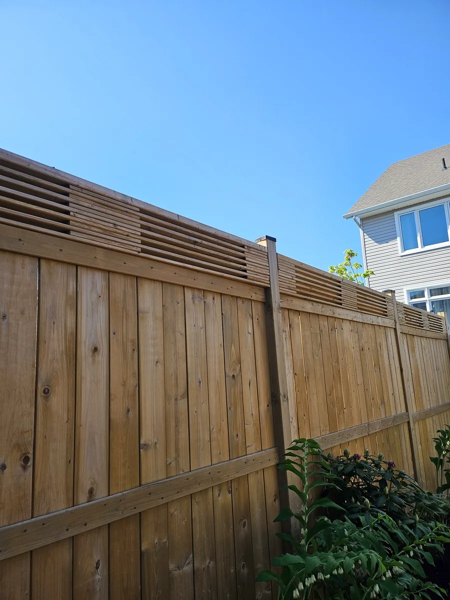 Corner of a privacy fence where two runs meet, showing the horizontal slat topper against the sky