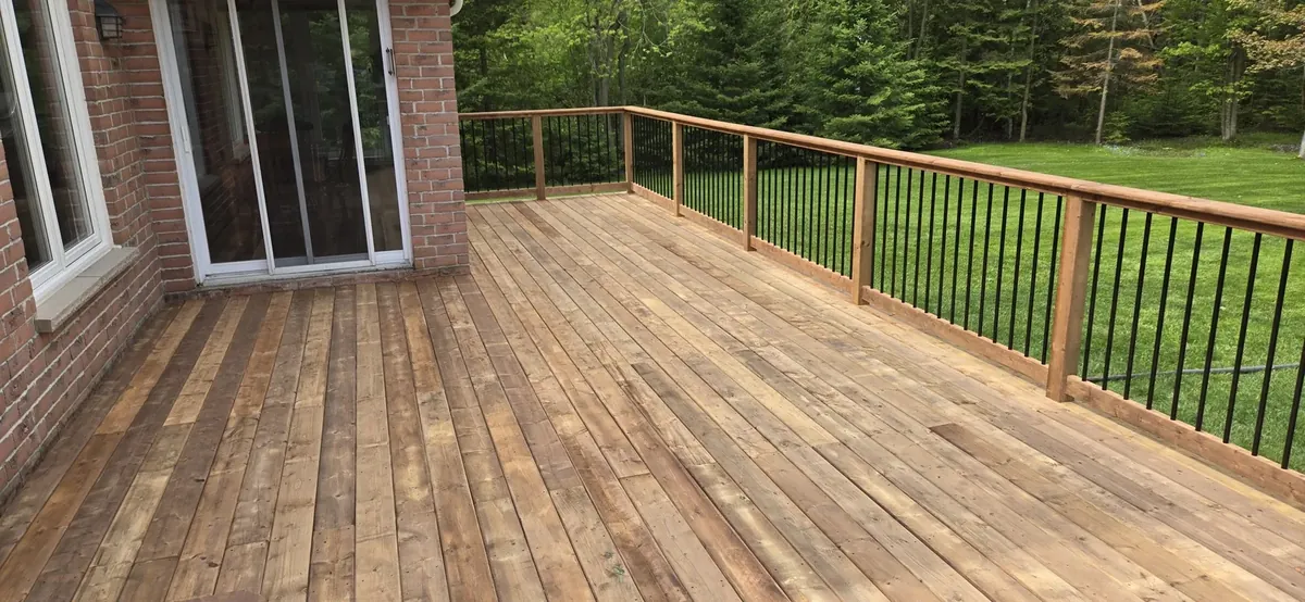 Cedar-tone pressure-treated deck with black aluminum railings built by XP Decking on a treed lot