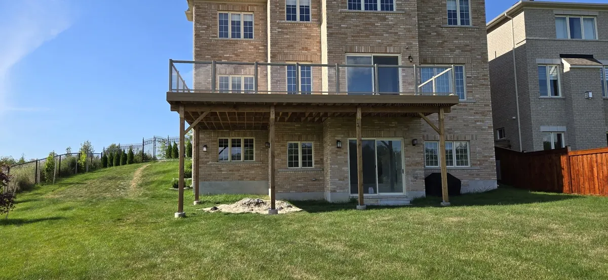 Elevated deck with glass panels across the back of a brick house, built by XP Decking