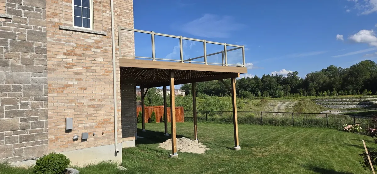 Elevated deck on tall posts with a glass railing on a brick home, built by XP Decking