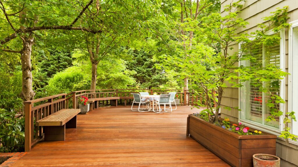 Spacious wooden backyard deck with built-in benches, patio furniture, and lush greenery showing the best time to build a deck in Newmarket Ontario.